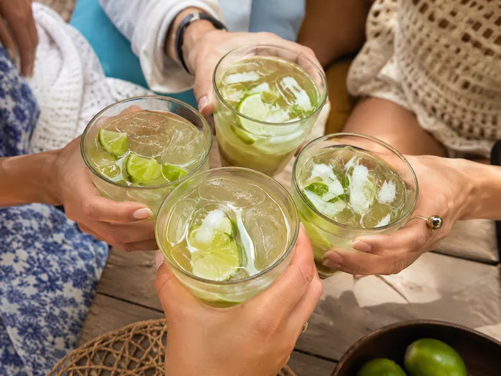 Hands raising caipirinha glasses together over a table