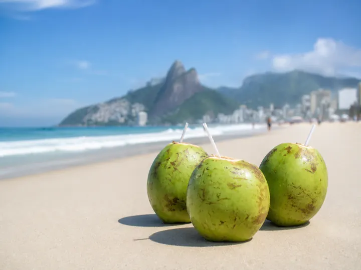 Fresh coconuts with straws on the sand at Ipanema beach